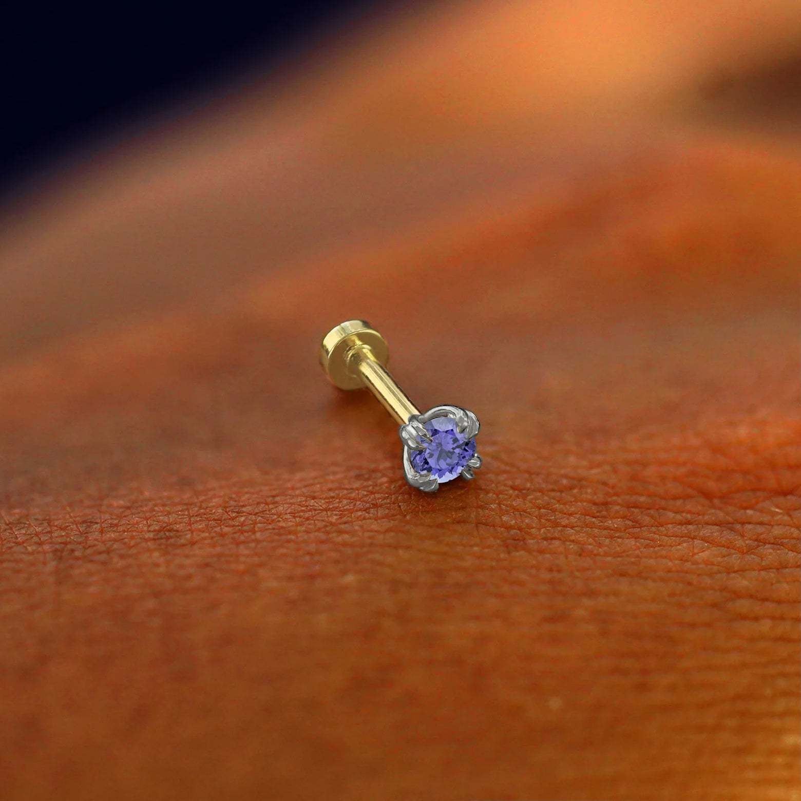 A solid 14k white gold Tanzanite Flatback Piercing resting on the back of a model's hand