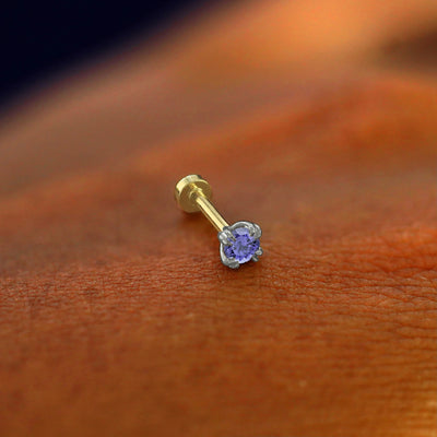 A solid 14k white gold Tanzanite Flatback Piercing resting on the back of a model's hand