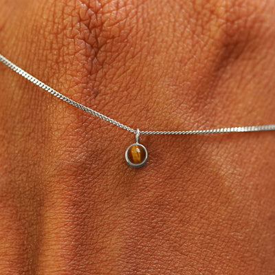 Close up view of a 14k white gold Tiger Eye Necklace draped across the back of a model's hand