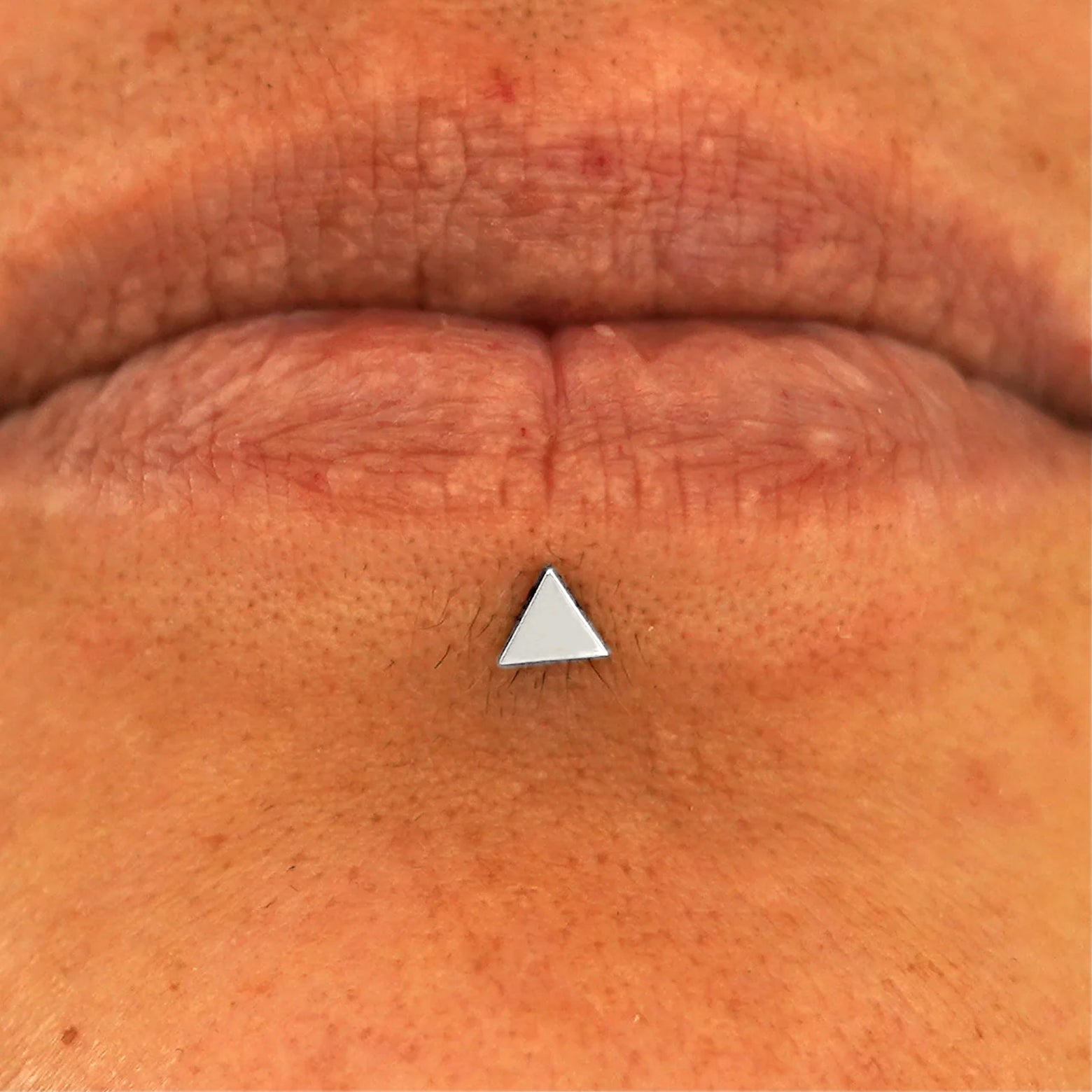 Close up view of a model's lips wearing a 14k white gold Triangle Flatback in a labret piercing
