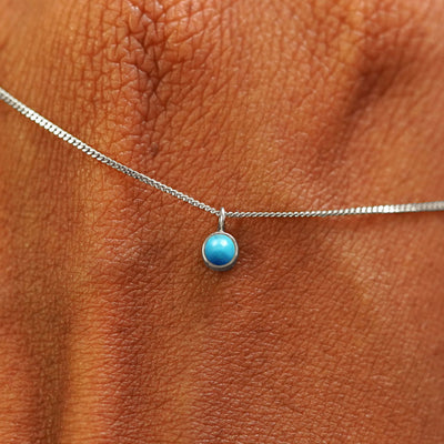 Close up view of a 14k white gold Turquoise Necklace draped across the back of a model's hand
