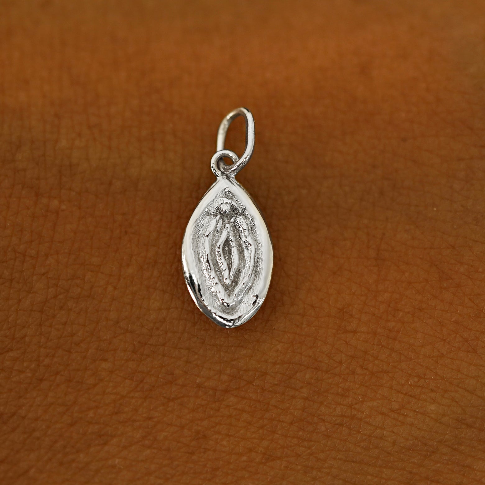 A solid 14k white gold Vulva Charm resting on the back of a model's hand