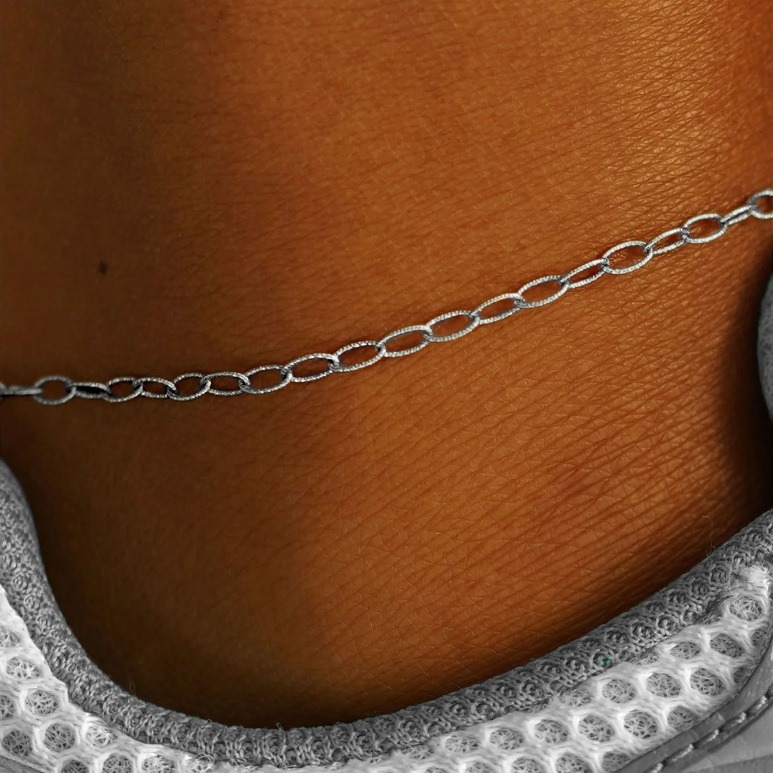 Close up view of a model's ankle wearing a solid white gold Veren Anklet