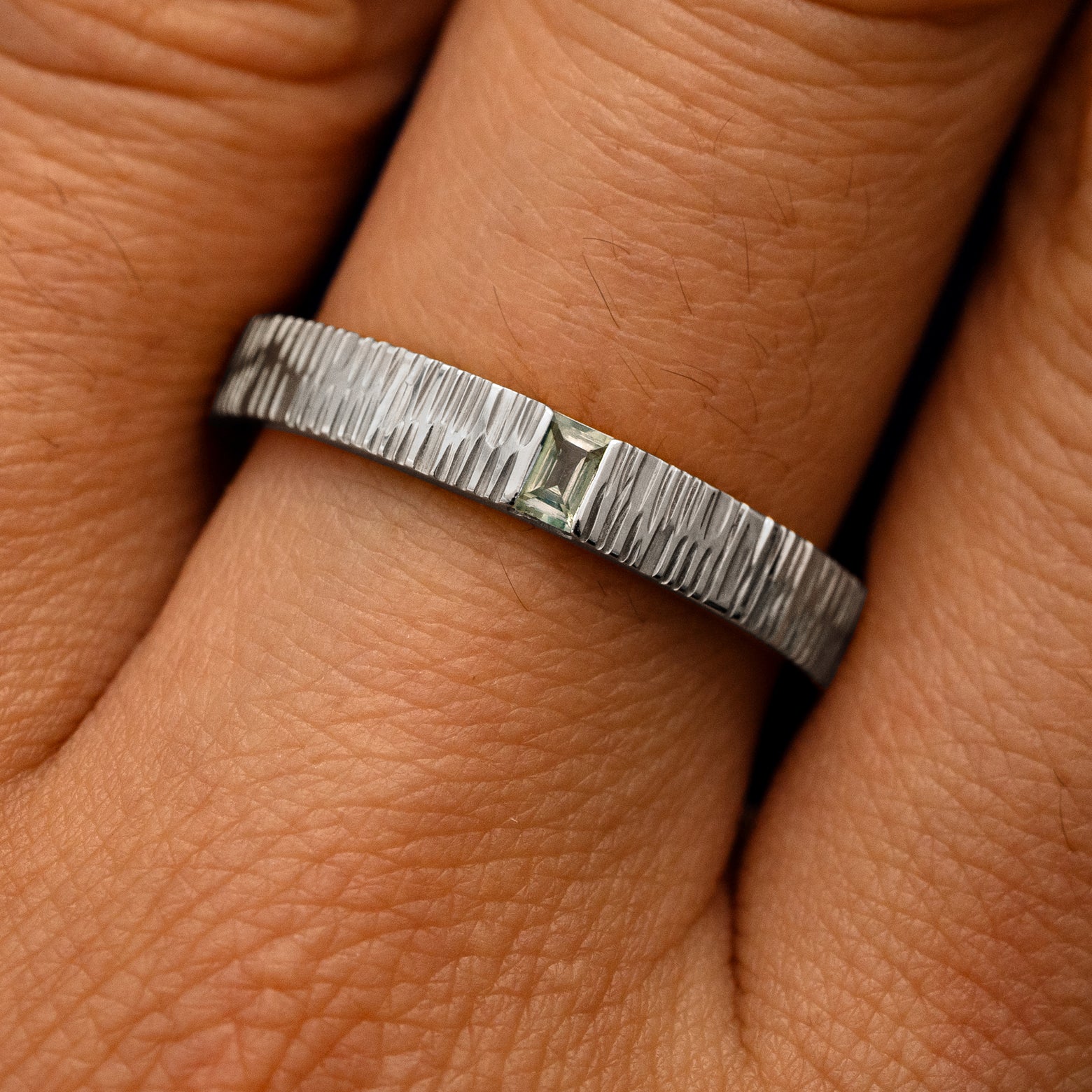 Close up view of a model's fingers wearing a white gold Baguette Green Sapphire Wood Band