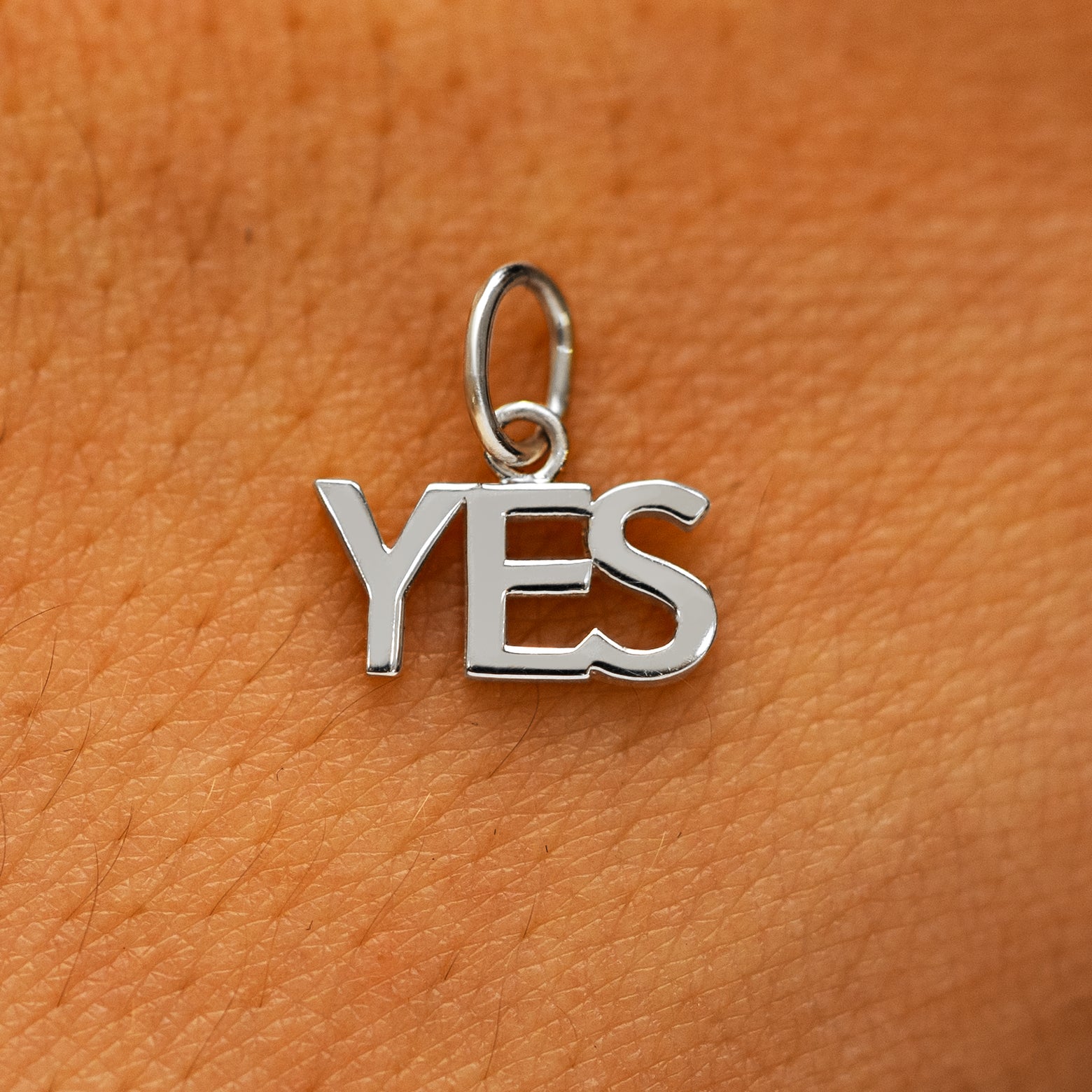 A solid 14k white gold Yes Charm on the back of a models hand