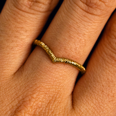 Close up view of a model's fingers wearing a 14k yellow gold wood finish Chevron Band
