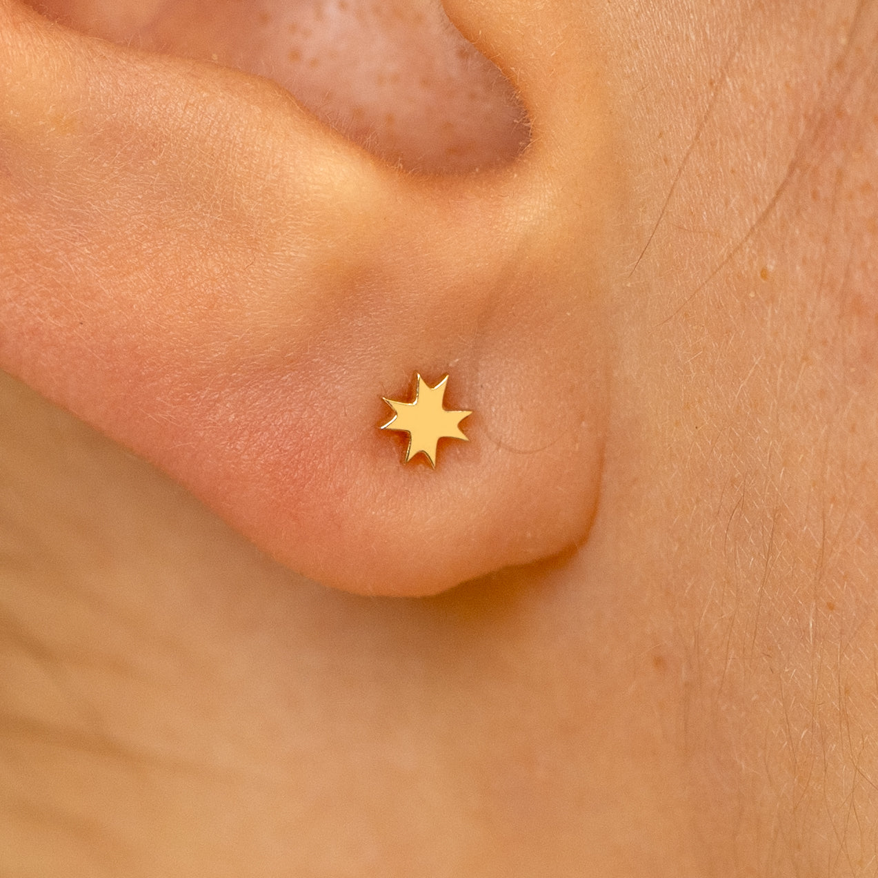 Close up view of a models ear wearing a 14k yellow gold 8 pointed star flatback piercing