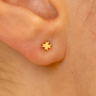 Close up view of a models ear wearing a 14k yellow gold 8 pointed star flatback piercing