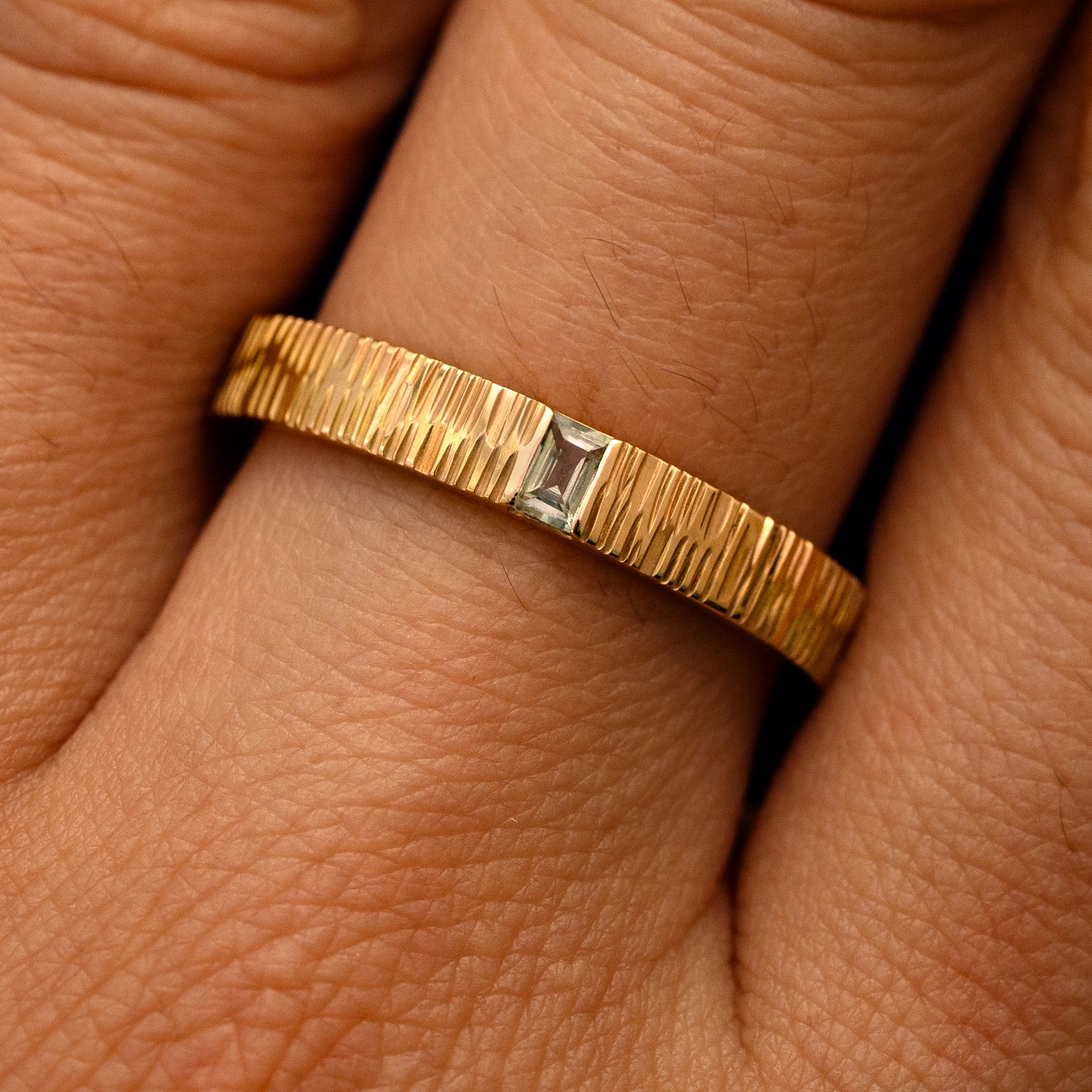 Close up view of a model's fingers wearing a 14k yellow gold Baguette Green Sapphire Wood Band