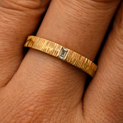 Close up view of a model's fingers wearing a 14k yellow gold Baguette Green Sapphire Wood Band