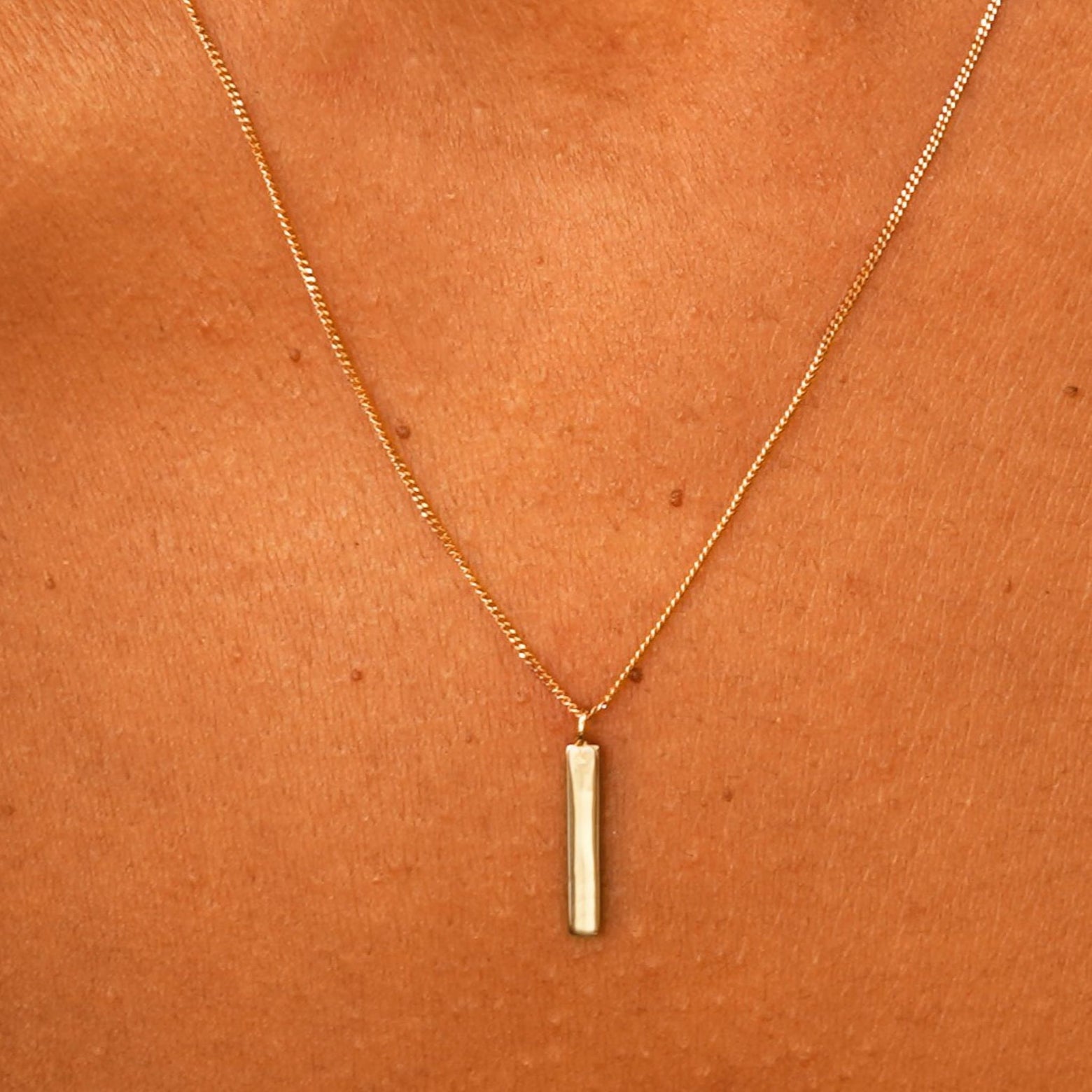 Close up view of a model's neck wearing a solid yellow gold Bar Necklace