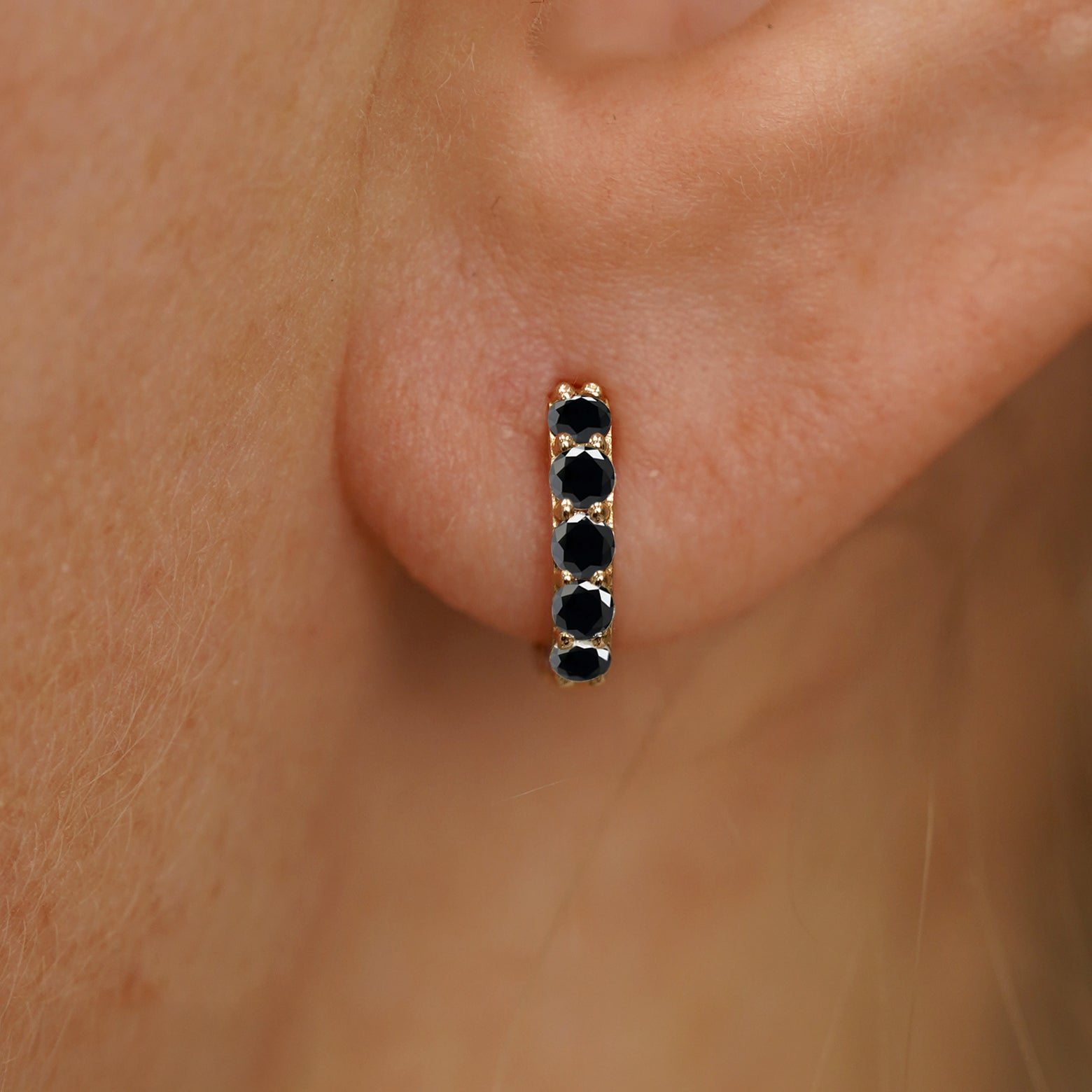Close up view of a model's ear wearing a yellow gold mini Black Diamond Huggie Hoop