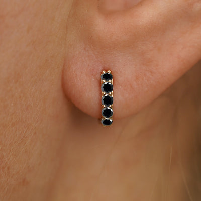 Close up view of a model's ear wearing a yellow gold mini Black Diamond Huggie Hoop