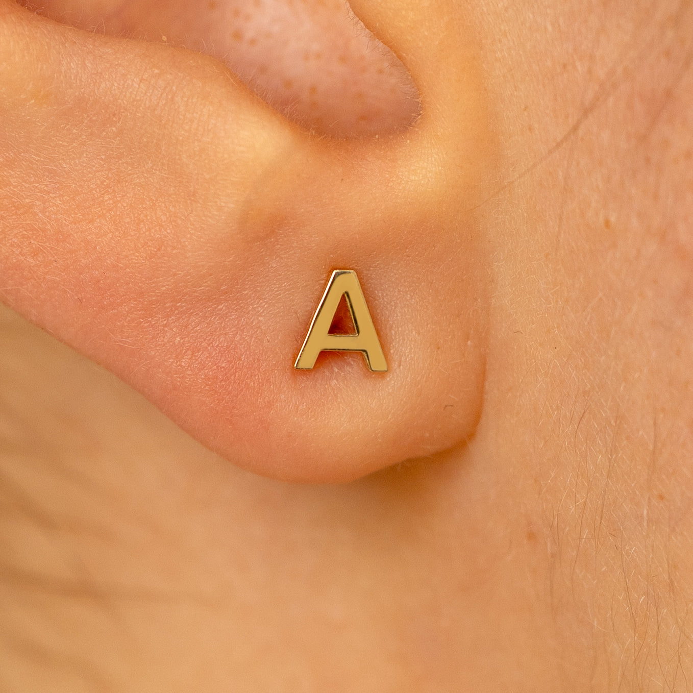 Close up view of a models ear wearing a 14k yellow gold block initial letter A stud earring