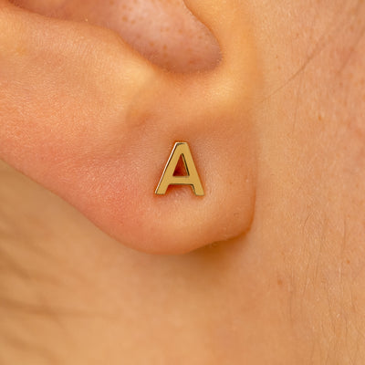 Close up view of a models ear wearing a 14k yellow gold block initial letter A stud earring