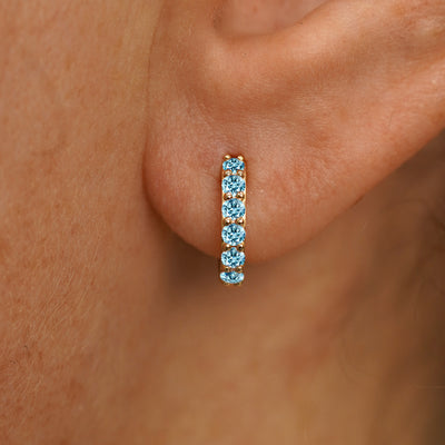 Close up view of a model's ear wearing a yellow gold Small Light Blue Lab Diamond Huggie Hoop
