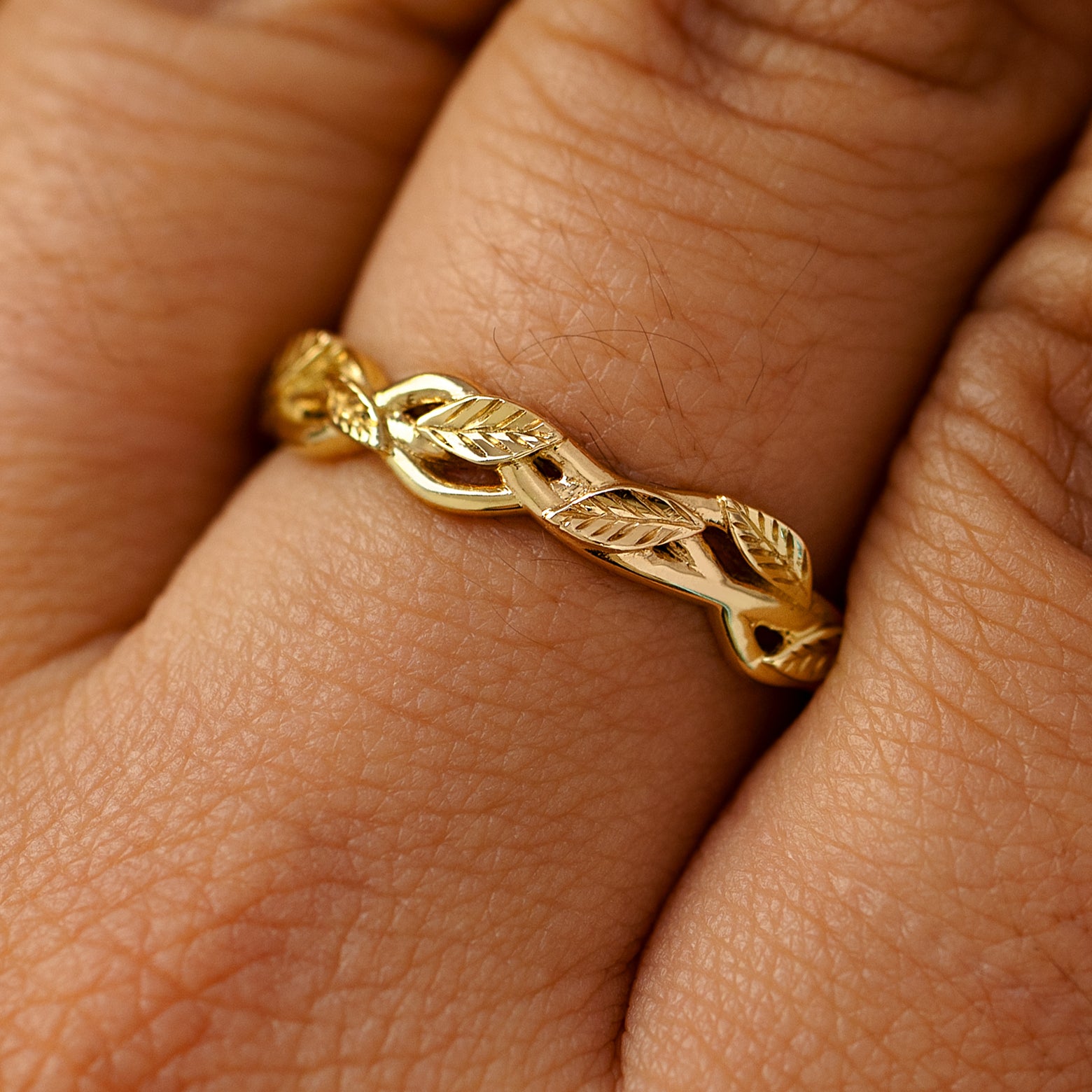 A solid 14k yellow gold braided leaves and vines ring on a model's finger