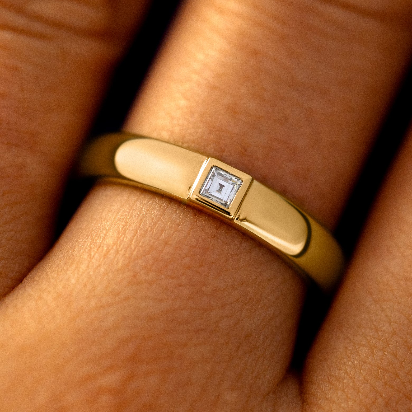 Close up view of a model's hand wearing a 14k yellow gold Square Carre Cut Diamond Band