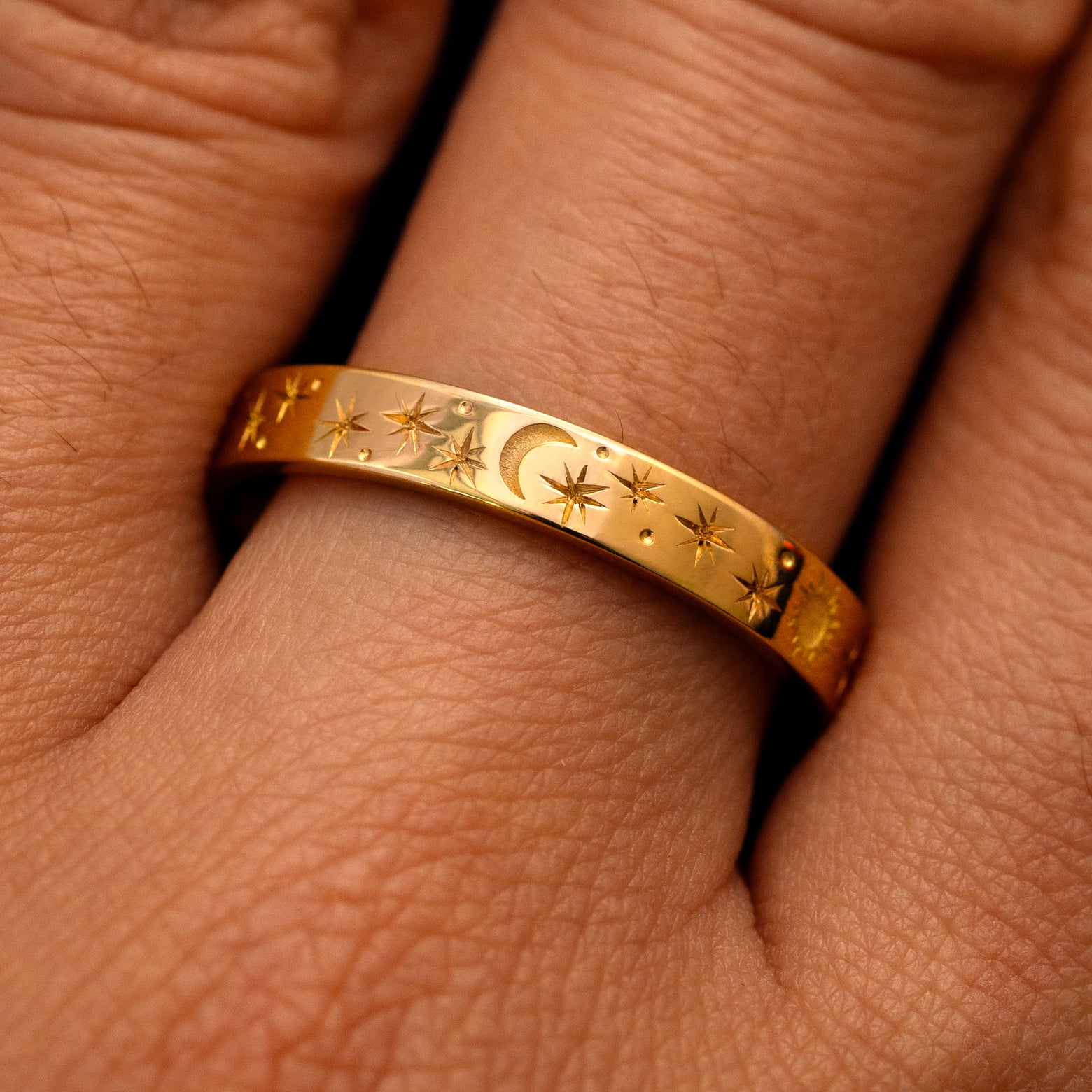 Close up view of a model's fingers wearing a 14k yellow gold Industrial Sun Moon and Stars Band