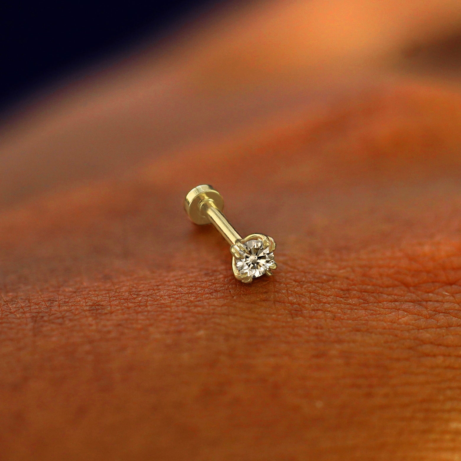 A solid 14k yellow gold Champagne Diamond Flatback Piercing resting on the back of a model's hand