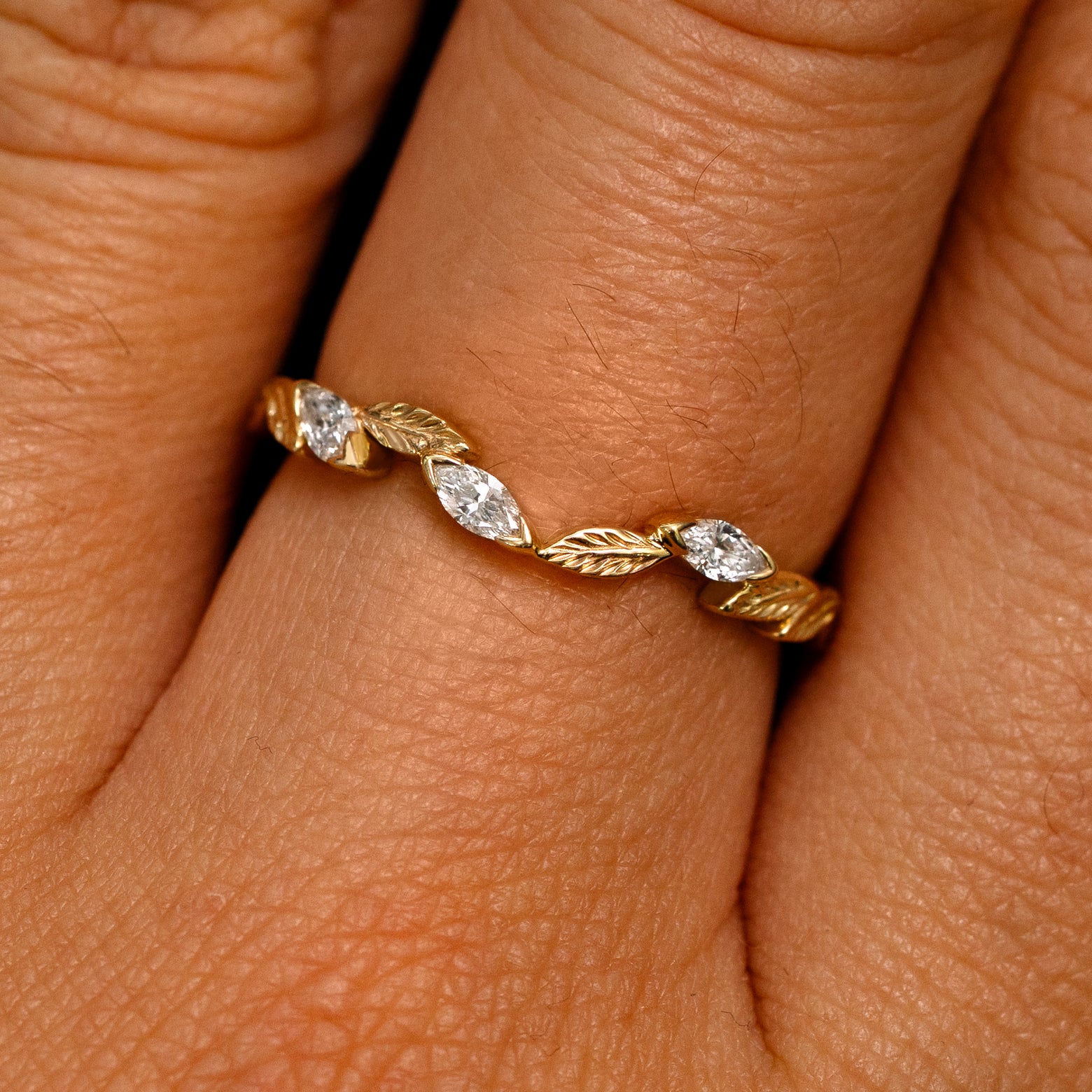 Close up view of a model's fingers wearing a 14k yellow gold Chevron Leaves and Marquise Diamonds Band