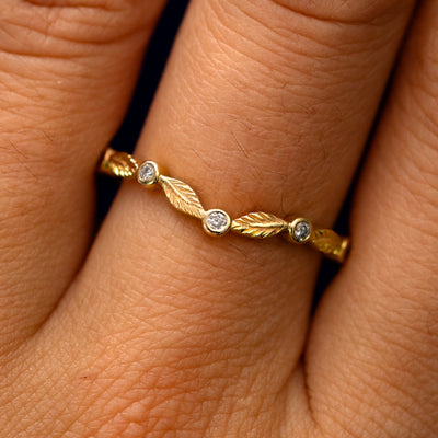 Close up view of a model's fingers wearing a 14k yellow gold Chevron Leaves and Round Diamonds Band