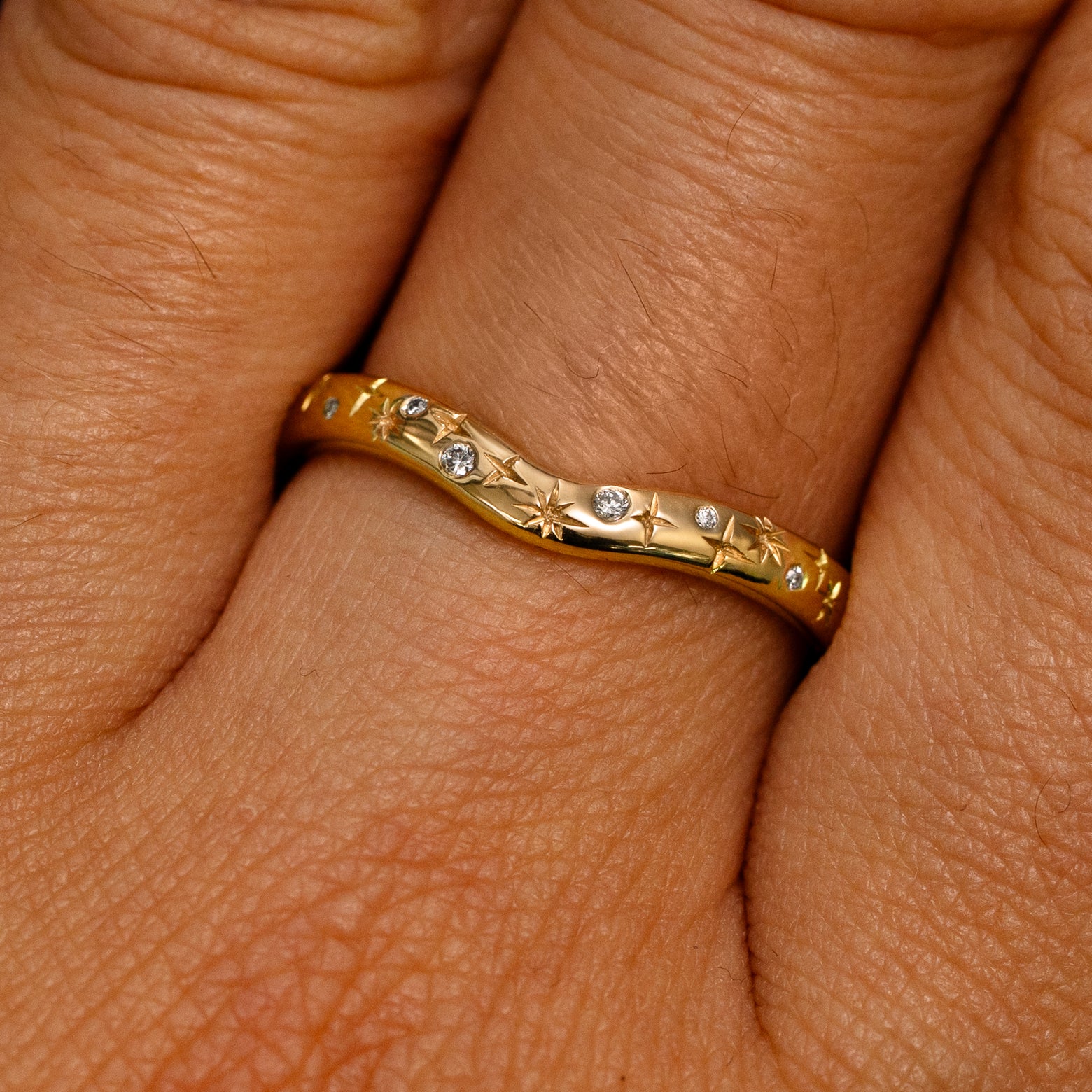 Close up view of a model's fingers wearing a 14k yellow gold Curvy Chevron Diamond Stars Band
