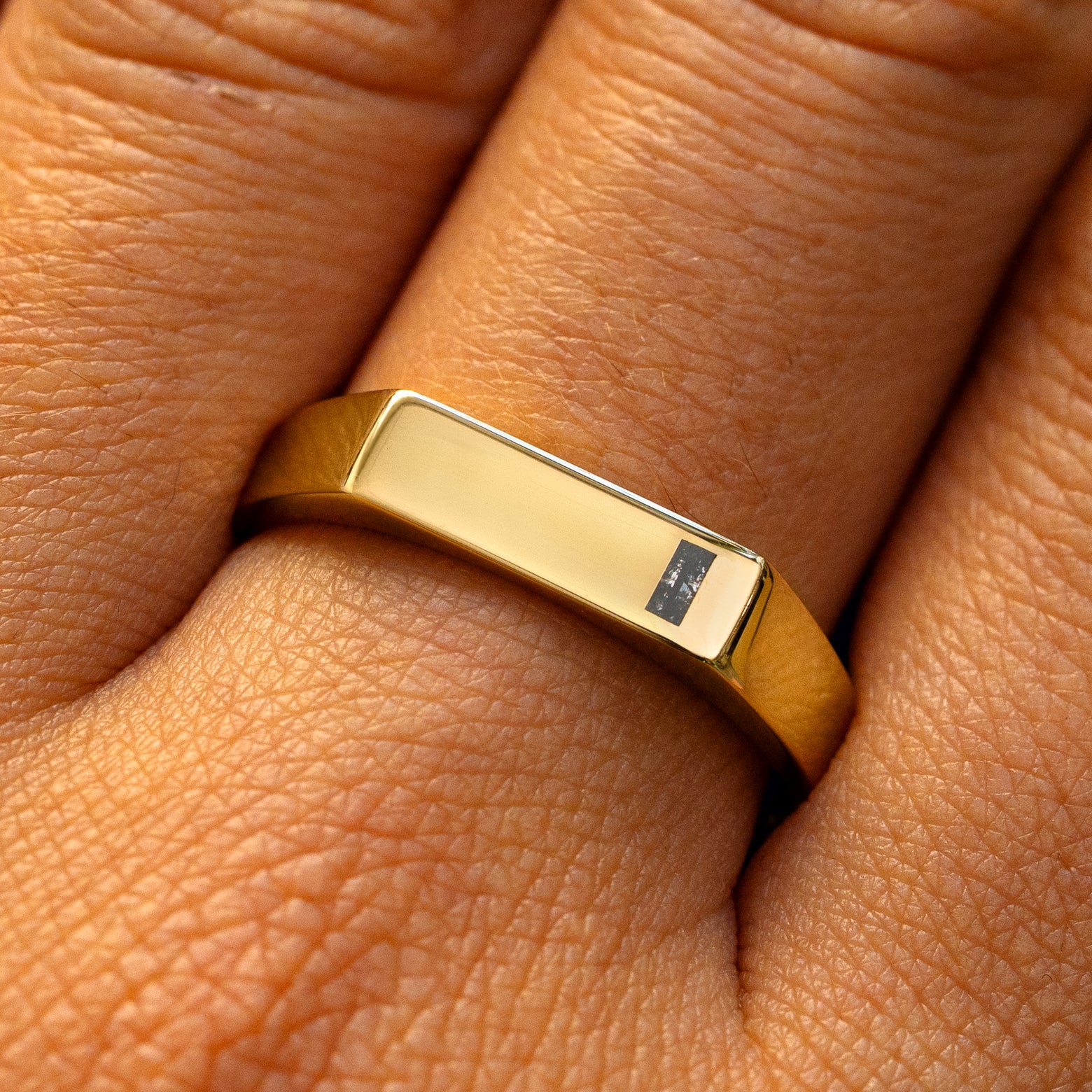 A model's finger wearing a yellow gold baguette salt and pepper diamond rectangular signet ring