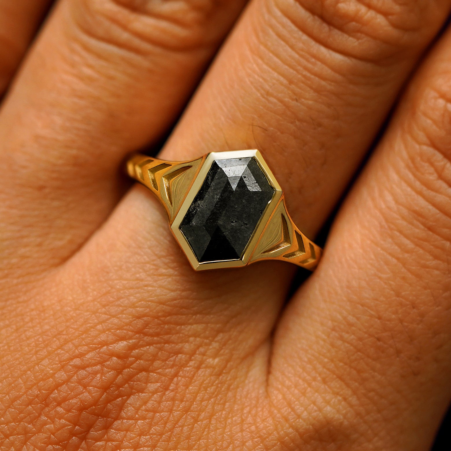 Close up view of a model's fingers wearing a 14k yellow gold elongated hexagon black diamond engraved chronos ring