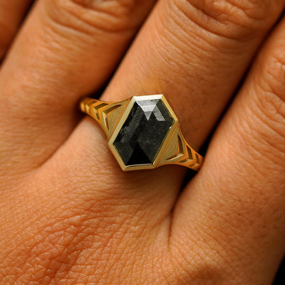 Close up view of a model's fingers wearing a 14k yellow gold elongated hexagon black diamond engraved chronos ring
