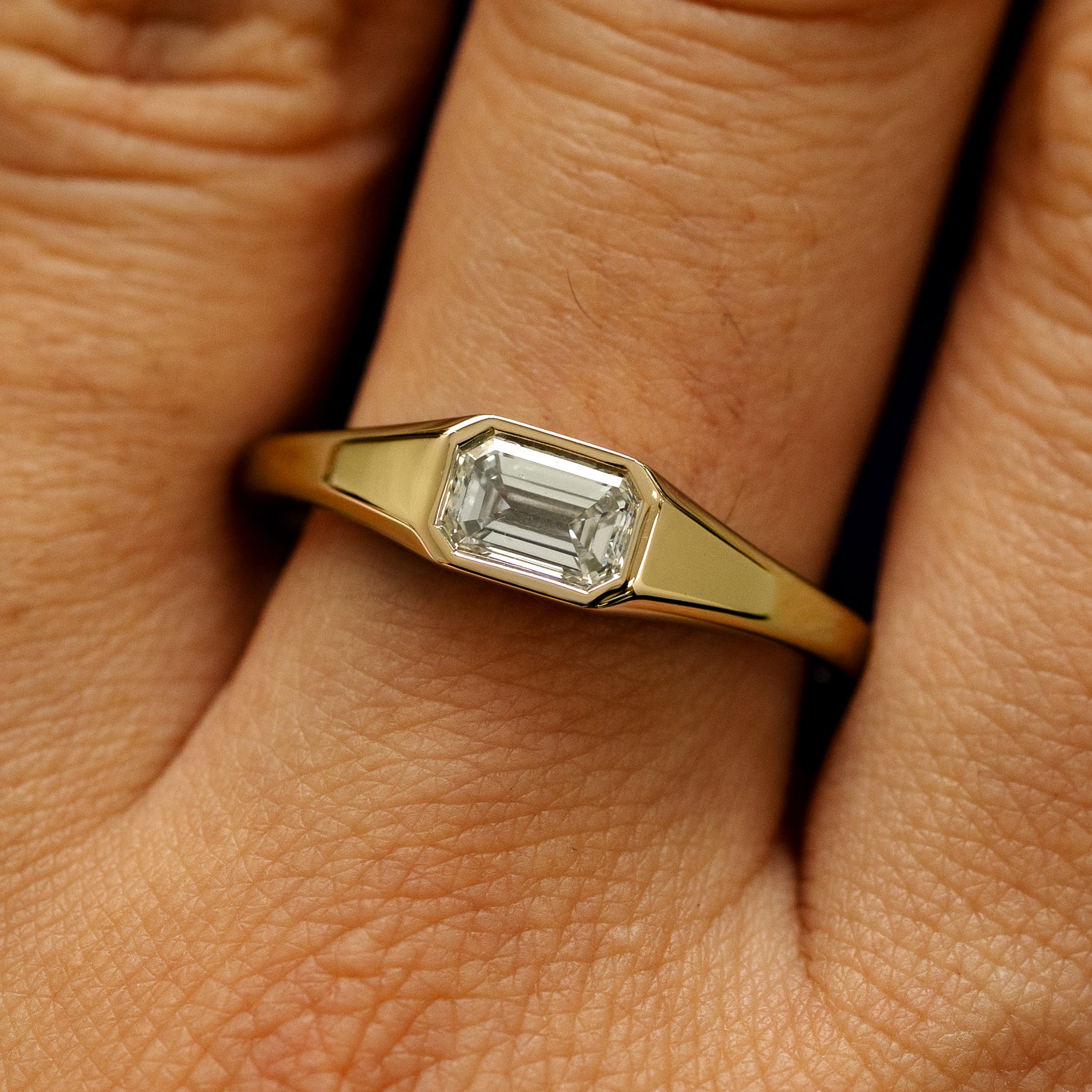Close up view of a model's fingers wearing a 14k yellow gold Emerald Cut Lab Created Diamond Signet Ring