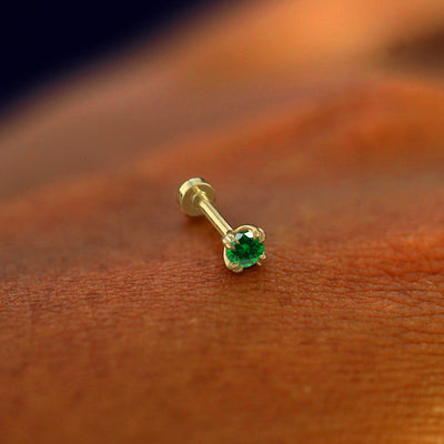A solid 14k yellow gold emerald Flatback Piercing resting on the back of a model's hand