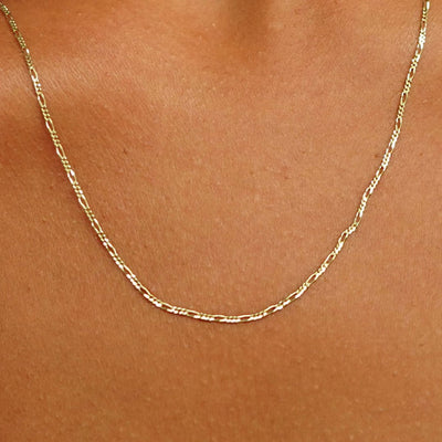 Close up view of a model's neck wearing a solid yellow gold Figaro Chain