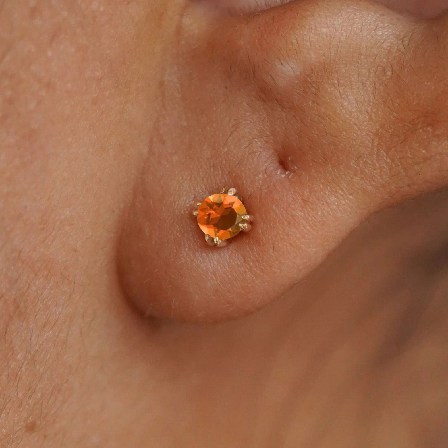 Close up view of a model's ear wearing a 14k yellow gold orange Fire Opal Earring