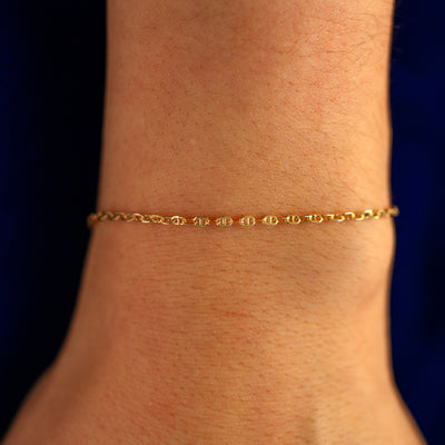 Close up view of a models wrist wearing a solid 14k yellow gold Flat Mariner Chain Bracelet