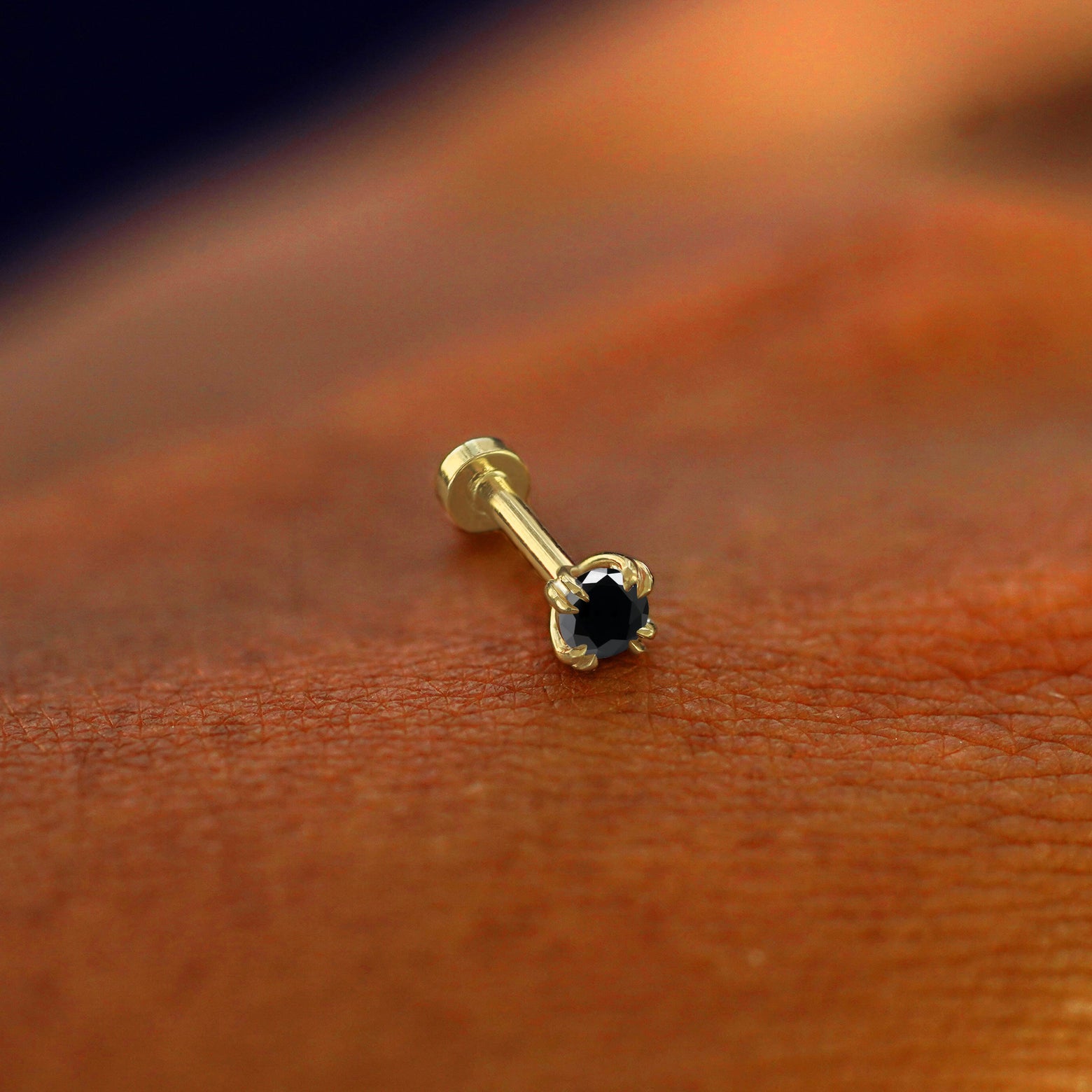 A solid 14k yellow gold Black Diamond Flatback Piercing resting on the back of a model's hand