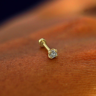 A solid 14k yellow gold Diamond Flatback Piercing resting on the back of a model's hand