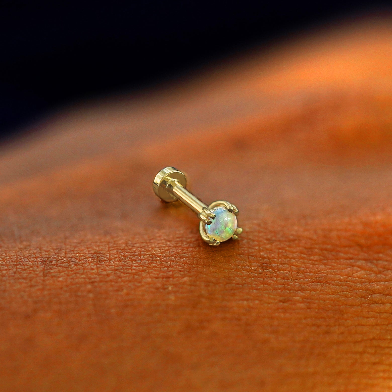 A solid 14k yellow gold Opal Flatback Piercing resting on the back of a model's hand