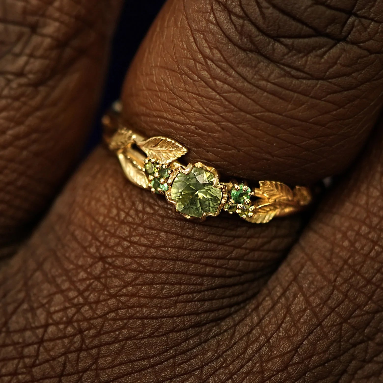 Close up view of a model's fingers wearing a 14k yellow gold Green Sapphire Leaves and Vines Ring