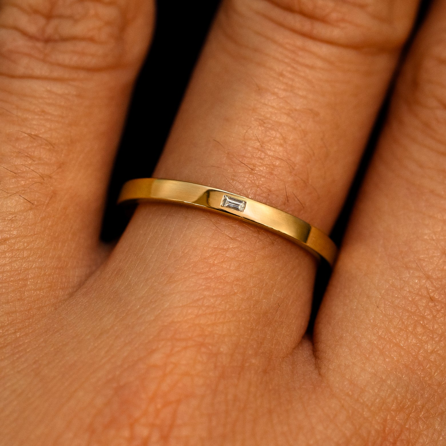 A 14k yellow gold Flush Set Baguette Diamond Ring on a model's finger