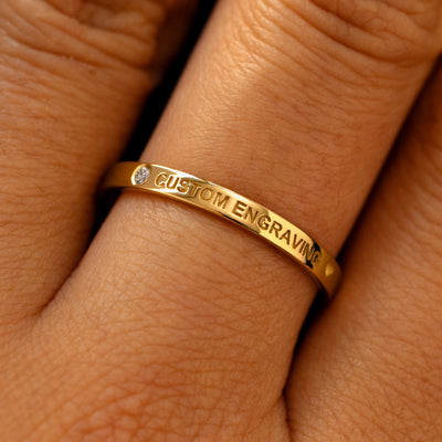 A model's finger wearing a diamond yellow gold flush gemstone industrial band the words custom engraving on the top