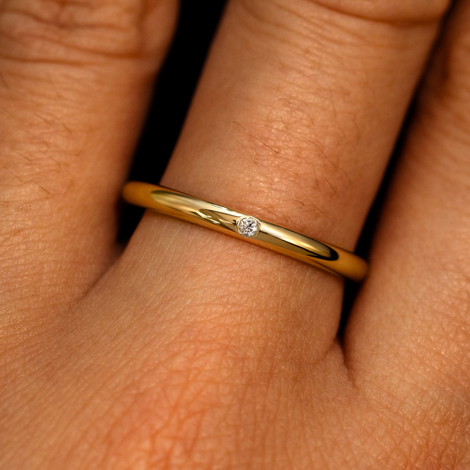 A 14k yellow gold Flush Set Round Diamond Ring on a model's finger