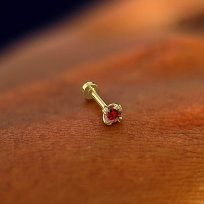 A solid 14k yellow gold Garnet Flatback Piercing resting on the back of a model's hand