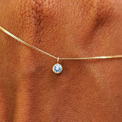 Close up view of a 14k yellow gold Aquamarine Necklace draped across the back of a model's hand