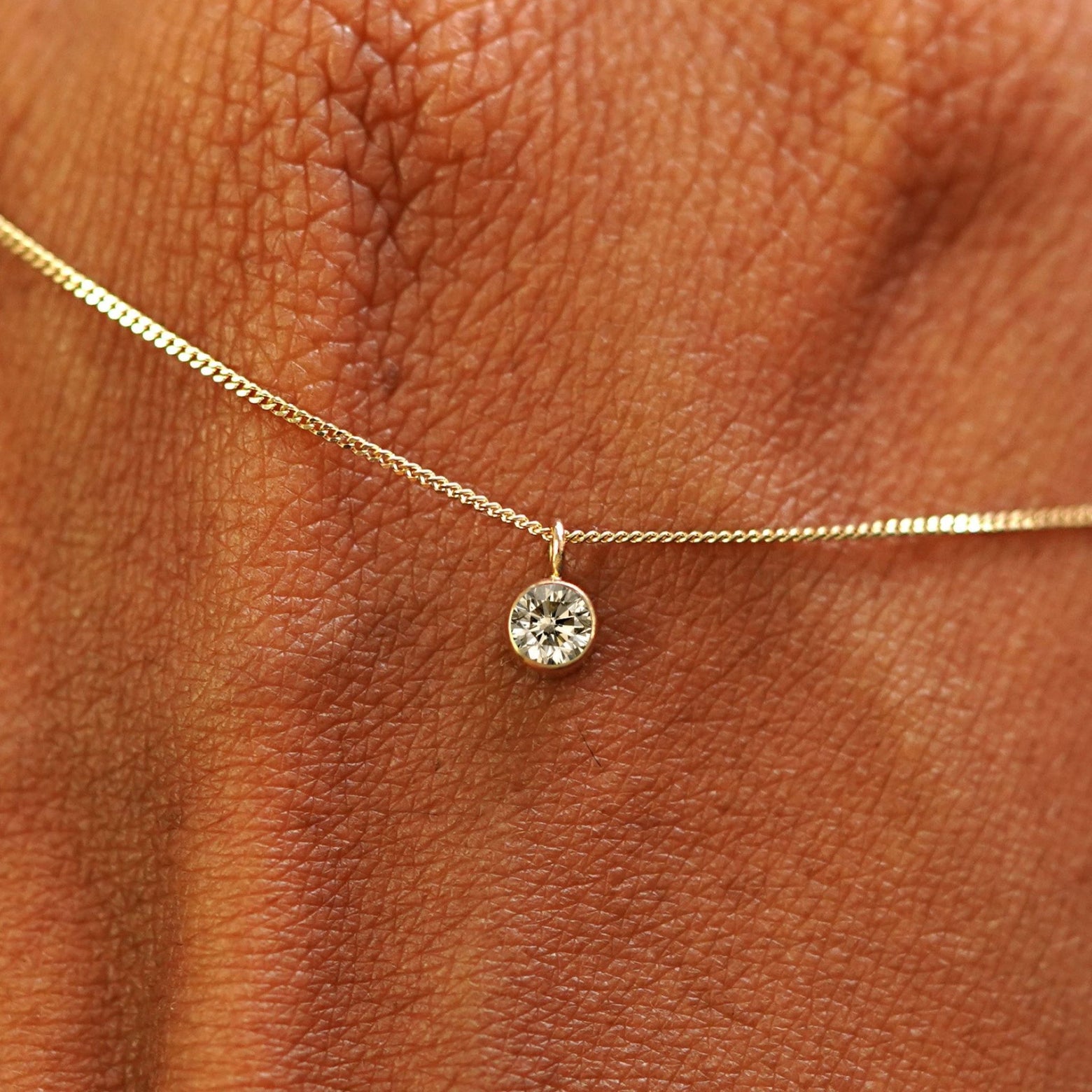 Close up view of a 14k yellow gold Champagne Diamond Necklace draped across the back of a model's hand