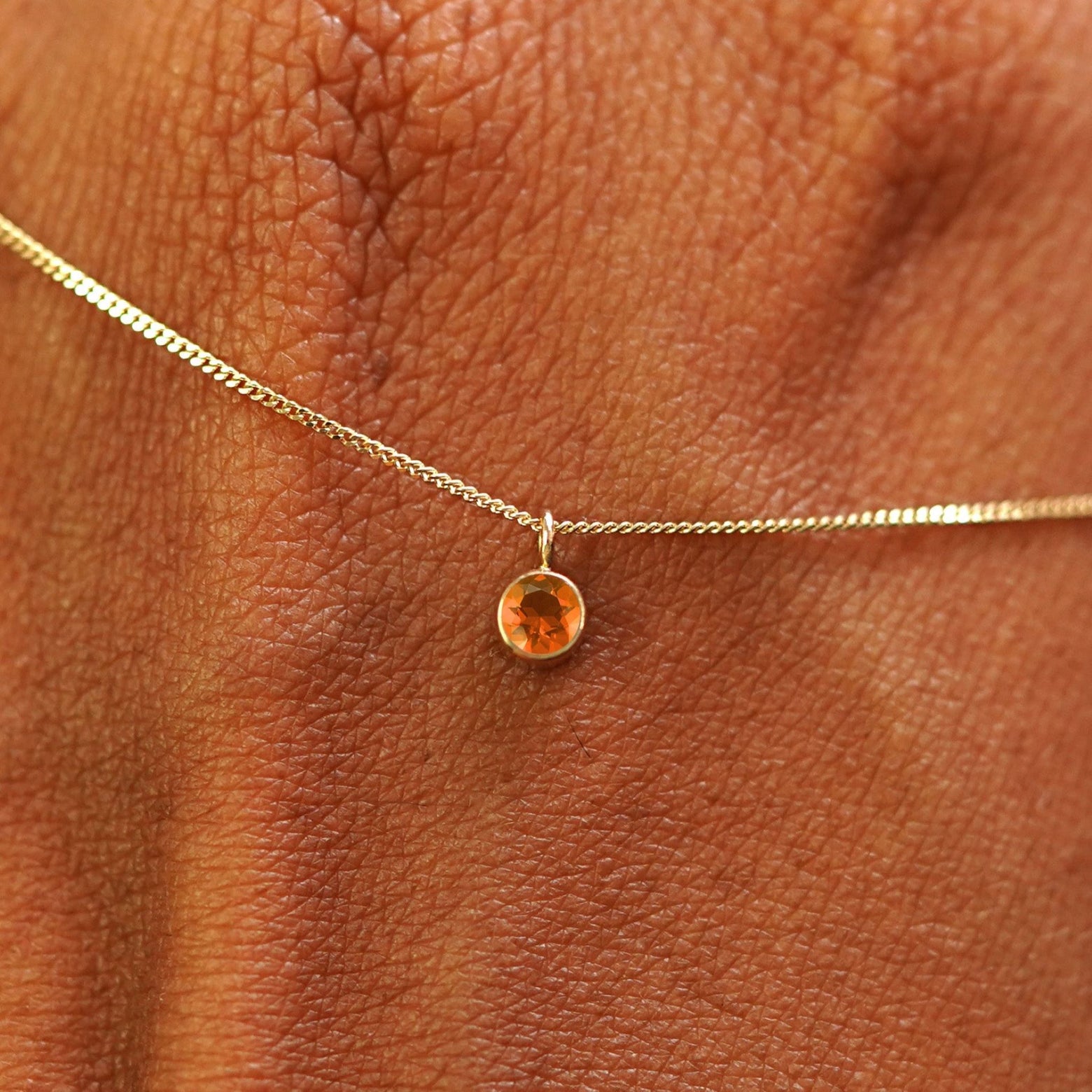 Close up view of a 14k yellow gold Fire Opal Necklace draped across the back of a model's hand