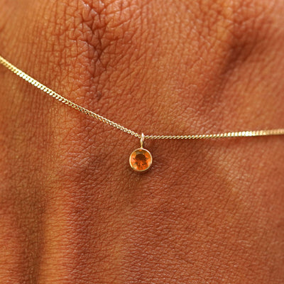 Close up view of a 14k yellow gold Fire Opal Necklace draped across the back of a model's hand