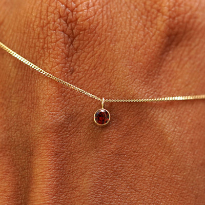 Close up view of a 14k yellow gold Garnet Necklace draped across the back of a model's hand