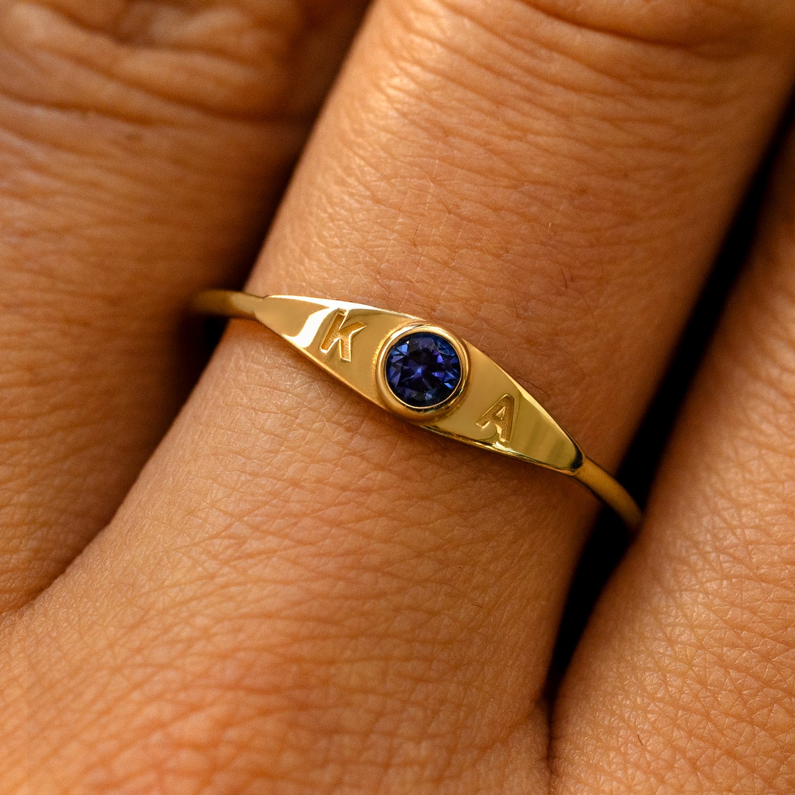 A model's finger wearing a sapphire yellow gold gemstone monogram ring with the initials K A