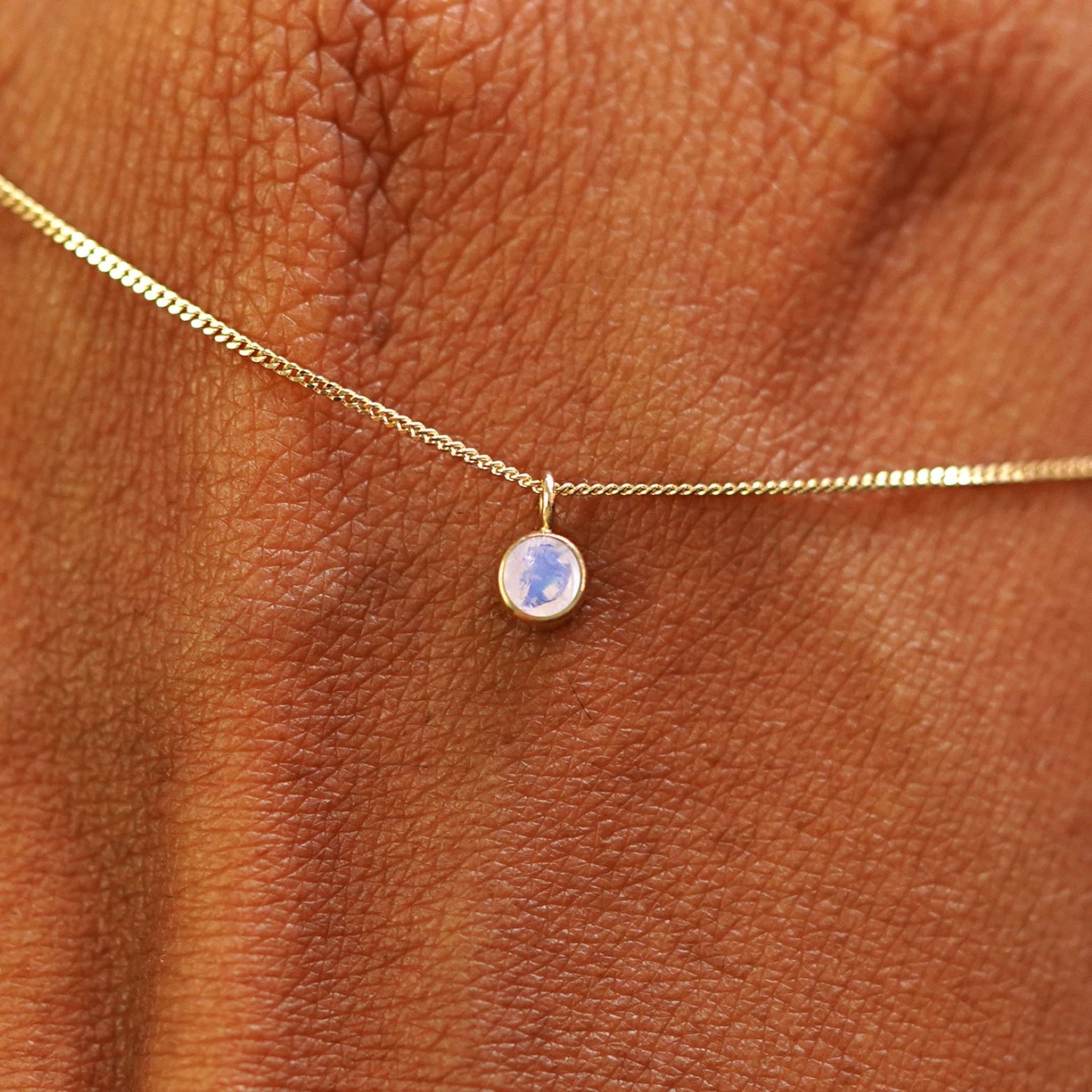 Close up view of a 14k yellow gold Moonstone Necklace draped across the back of a model's hand